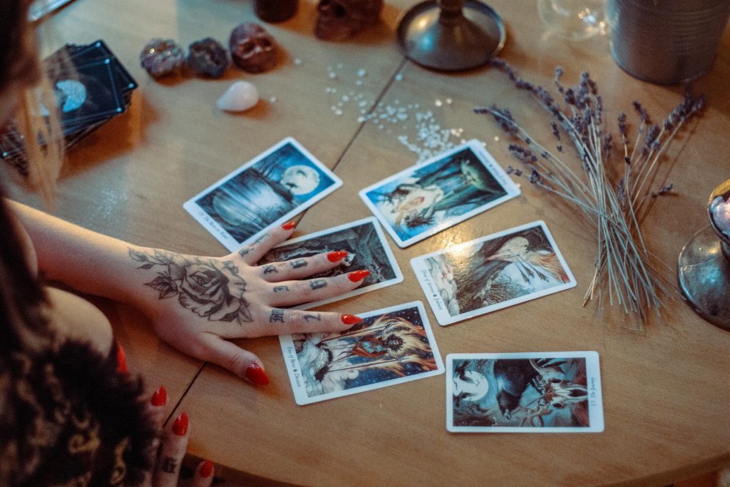 pexels-photo-3088369-3088369-1 A mystical setup featuring tarot card reading on a wooden table, with artistic tattoos and dried flowers.