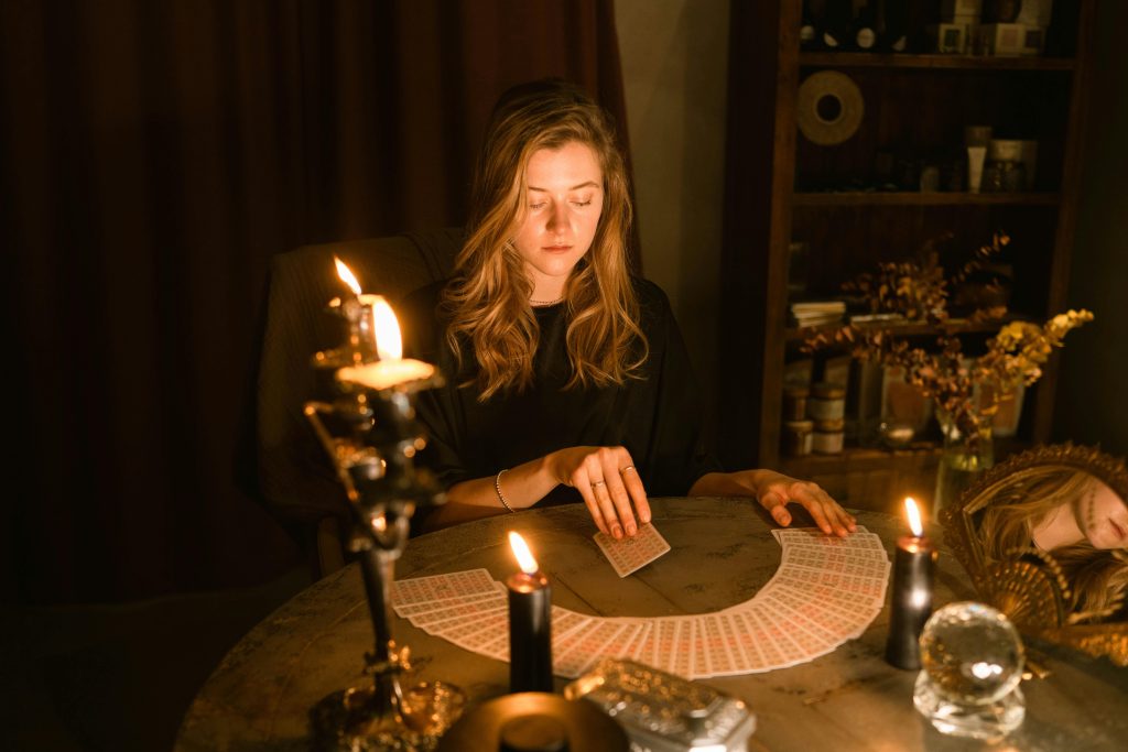 pexels-photo-6014317-6014317 A woman sitting in a dimly lit room, reading tarot cards by candlelight.